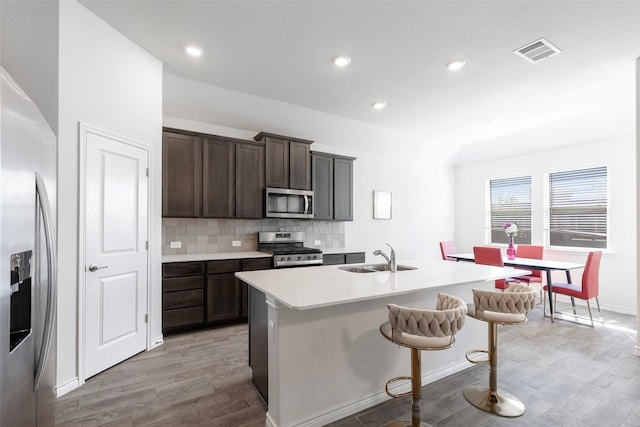 kitchen with an island with sink, appliances with stainless steel finishes, sink, and backsplash