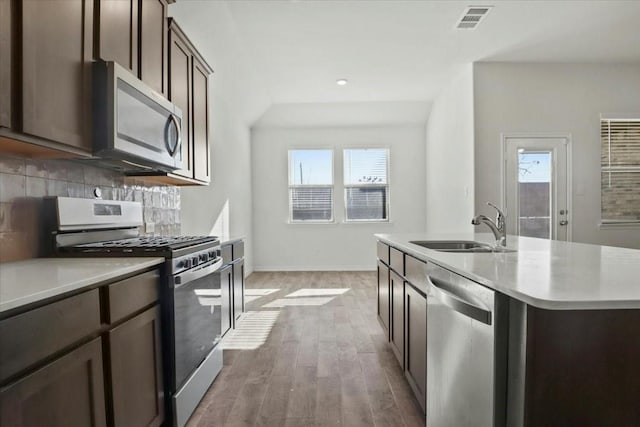 kitchen featuring appliances with stainless steel finishes, sink, decorative backsplash, hardwood / wood-style flooring, and a center island with sink