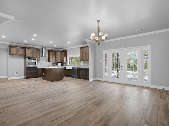 kitchen featuring appliances with stainless steel finishes, pendant lighting, light hardwood / wood-style floors, decorative backsplash, and wall chimney range hood