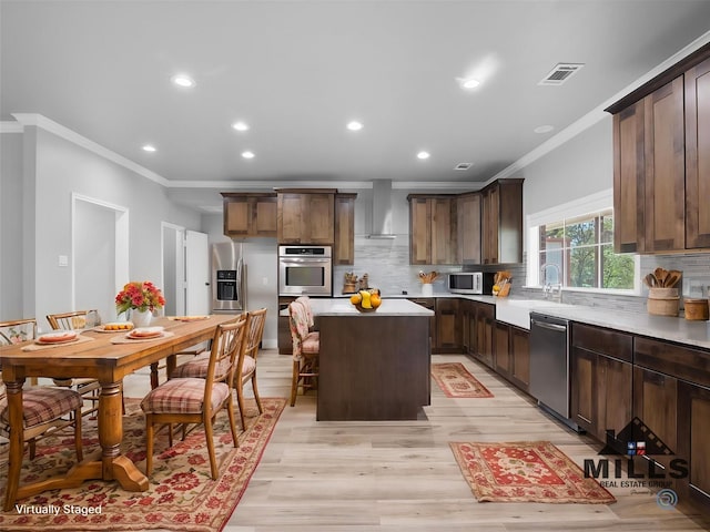 kitchen with sink, dark brown cabinets, a kitchen island, stainless steel appliances, and wall chimney range hood