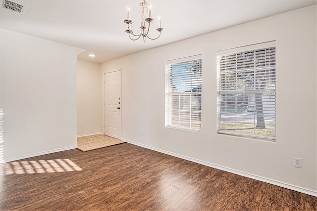 empty room with hardwood / wood-style floors, a healthy amount of sunlight, and a notable chandelier