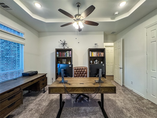 carpeted office space with ceiling fan and a raised ceiling