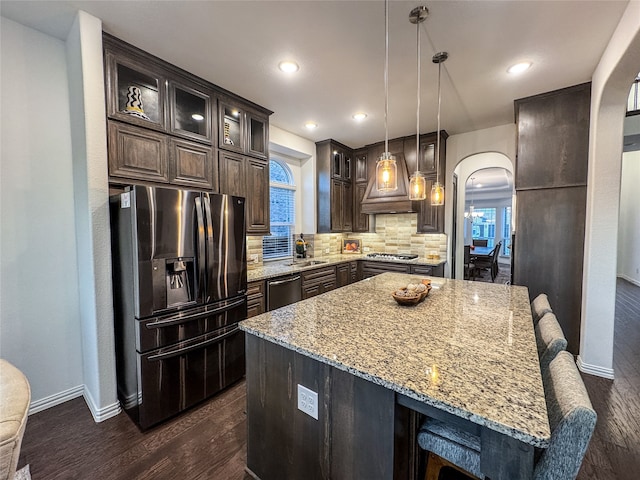 kitchen with dark wood-type flooring, a center island, decorative light fixtures, appliances with stainless steel finishes, and tasteful backsplash