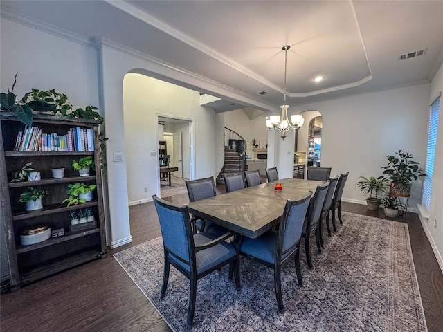 dining area with a notable chandelier, a tray ceiling, ornamental molding, and dark hardwood / wood-style flooring