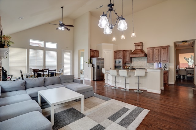 living room with dark wood-type flooring, ceiling fan with notable chandelier, and high vaulted ceiling