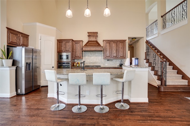 kitchen featuring a breakfast bar area, dark hardwood / wood-style floors, pendant lighting, a towering ceiling, and stainless steel appliances