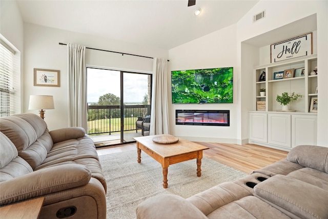 living area with lofted ceiling, light wood-type flooring, a glass covered fireplace, and visible vents