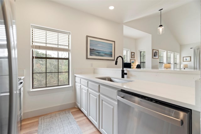 kitchen featuring light wood-type flooring, stainless steel dishwasher, sink, decorative light fixtures, and white cabinetry