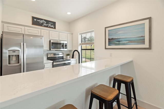 kitchen with white cabinetry, a kitchen breakfast bar, light stone counters, kitchen peninsula, and appliances with stainless steel finishes