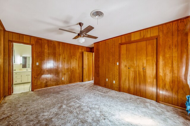 unfurnished bedroom with wood walls, ensuite bathroom, carpet, and ceiling fan