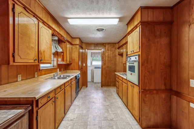 kitchen with oven, independent washer and dryer, wood walls, and sink