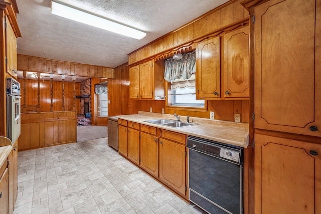 kitchen featuring oven, black dishwasher, sink, a textured ceiling, and wood walls