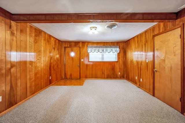 empty room with beamed ceiling, wood walls, and light colored carpet