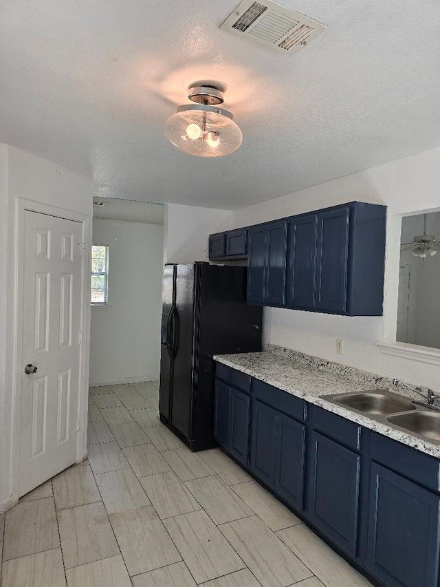 kitchen with sink, a textured ceiling, black fridge, ceiling fan, and blue cabinetry