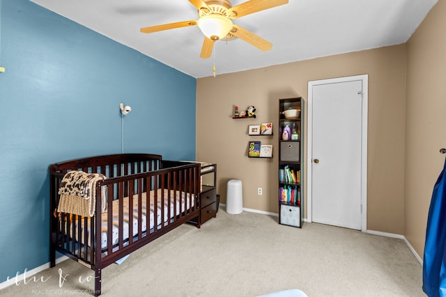 carpeted bedroom with a crib and ceiling fan