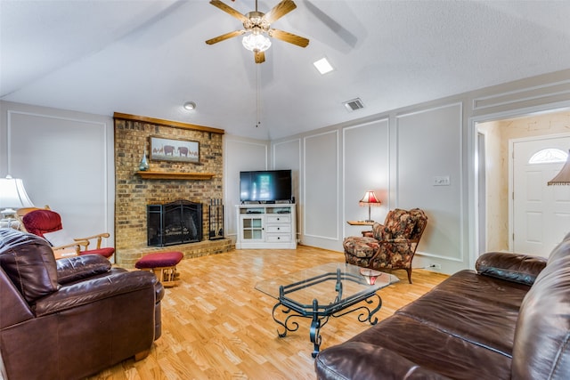 living room featuring ceiling fan, a textured ceiling, a brick fireplace, vaulted ceiling, and light hardwood / wood-style flooring