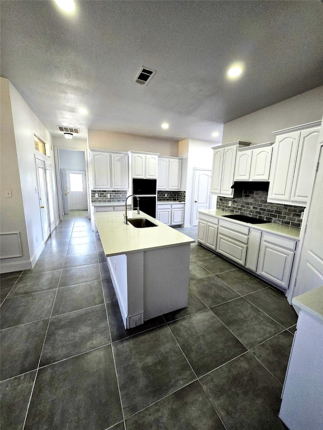 kitchen with sink, dark tile patterned flooring, an island with sink, decorative backsplash, and white cabinets