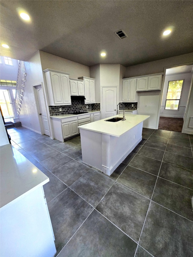 kitchen featuring stovetop, sink, white cabinetry, and an island with sink