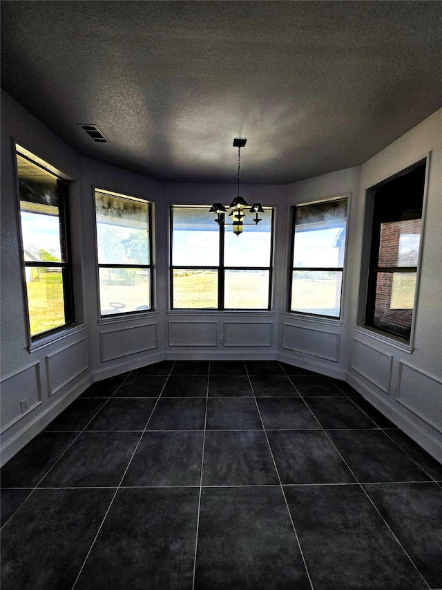 unfurnished dining area featuring dark tile patterned flooring, a textured ceiling, and an inviting chandelier