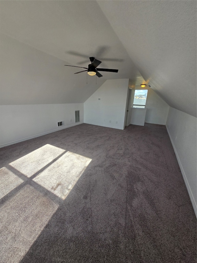 bonus room with ceiling fan, a textured ceiling, vaulted ceiling, and dark colored carpet