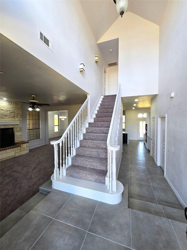 stairway with high vaulted ceiling, tile patterned flooring, and a stone fireplace