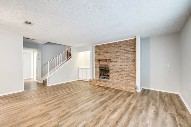 unfurnished living room with a brick fireplace, a textured ceiling, and light wood-type flooring