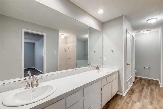 bathroom featuring hardwood / wood-style floors, a tile shower, a textured ceiling, toilet, and vanity