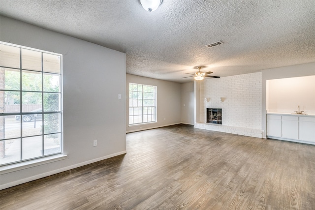 unfurnished living room featuring ceiling fan, hardwood / wood-style flooring, a textured ceiling, and a fireplace