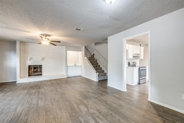 unfurnished living room with a textured ceiling, hardwood / wood-style flooring, ceiling fan, and a brick fireplace