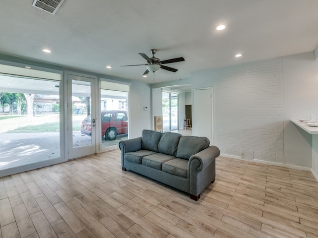 living room featuring ceiling fan, light hardwood / wood-style flooring, and brick wall