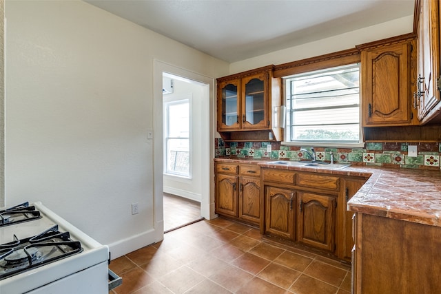 kitchen featuring tile countertops, sink, white range with gas stovetop, and backsplash