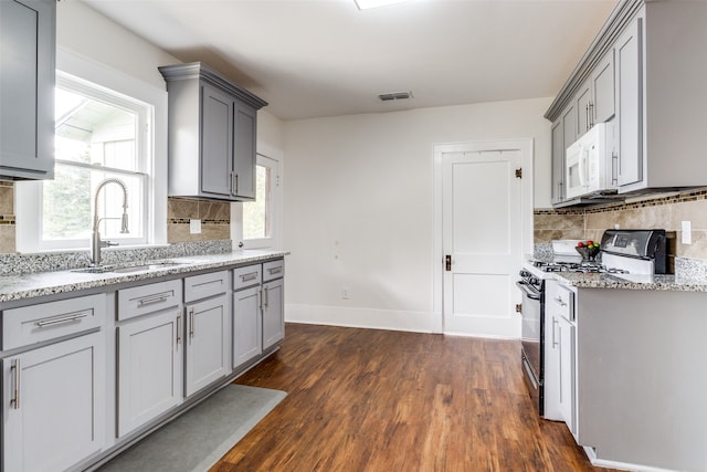 kitchen with light stone countertops, dark hardwood / wood-style flooring, gray cabinetry, gas stove, and sink