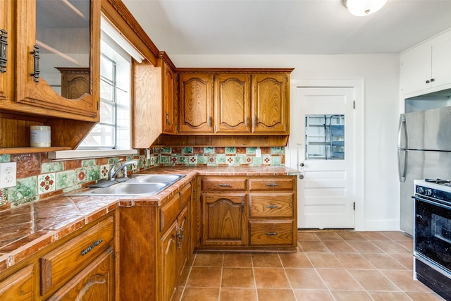 kitchen featuring stainless steel fridge, black stove, tasteful backsplash, sink, and light tile patterned floors