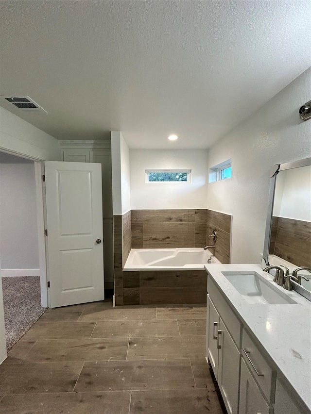 bathroom featuring a textured ceiling, a garden tub, vanity, visible vents, and wood tiled floor