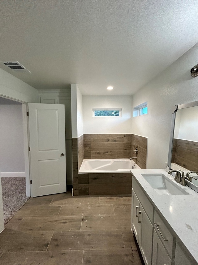 bathroom with vanity, wood-type flooring, a textured ceiling, and tiled tub