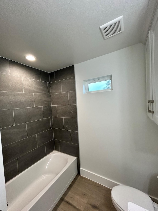 full bath with shower / tub combination, toilet, wood finished floors, visible vents, and baseboards