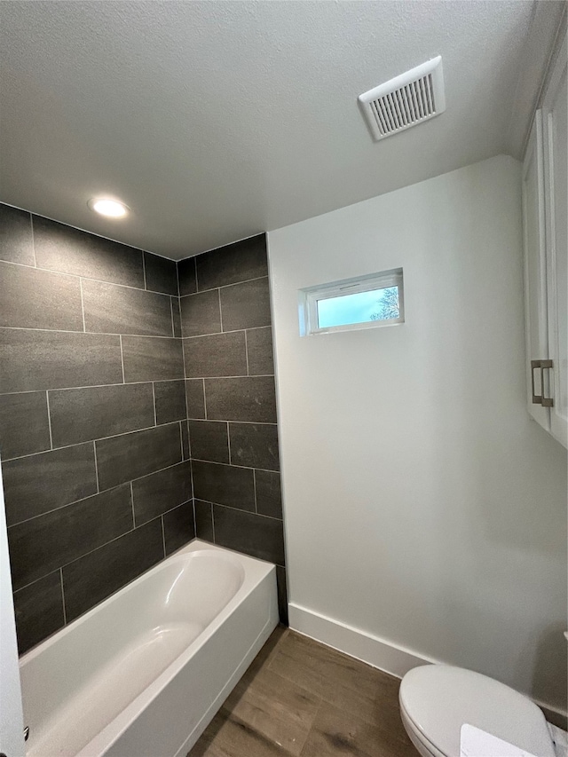 bathroom with toilet, hardwood / wood-style flooring, a textured ceiling, and tiled shower / bath