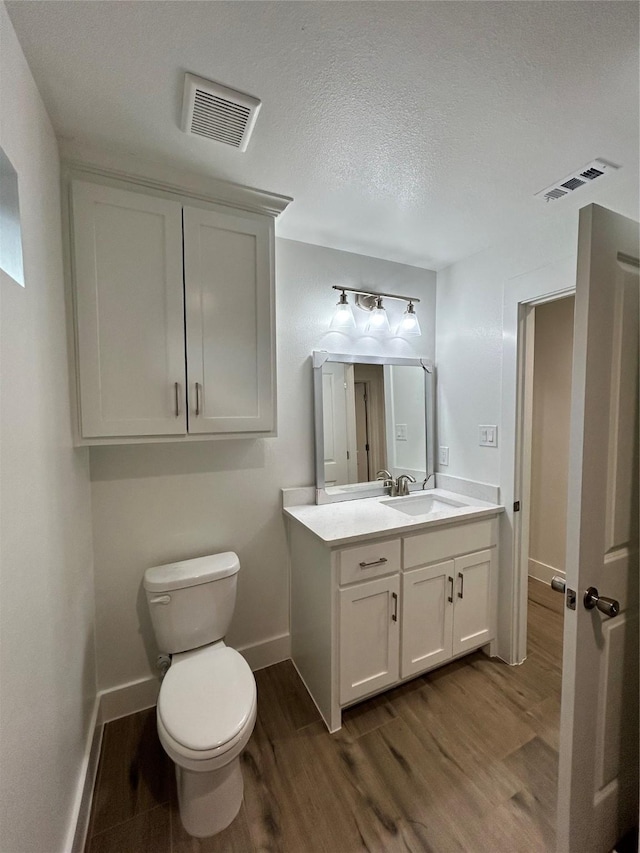 half bathroom featuring baseboards, visible vents, toilet, wood finished floors, and vanity