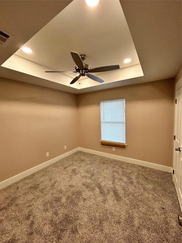 carpeted empty room with recessed lighting, a ceiling fan, visible vents, baseboards, and a tray ceiling