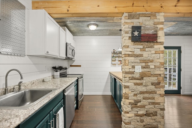 kitchen with appliances with stainless steel finishes, sink, white cabinetry, wooden walls, and dark wood-type flooring