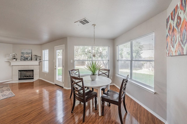 dining room featuring a tile fireplace, wood-type flooring, a textured ceiling, and an inviting chandelier