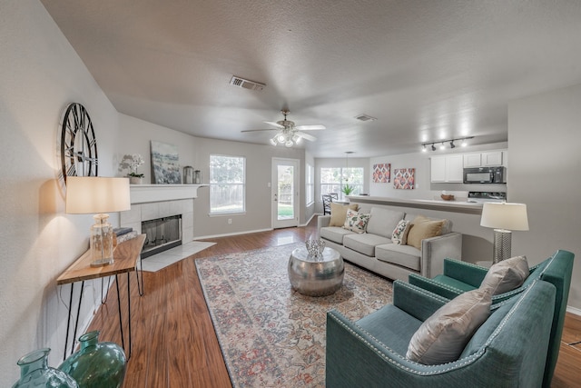 living room with ceiling fan, light wood-type flooring, a textured ceiling, and a tile fireplace