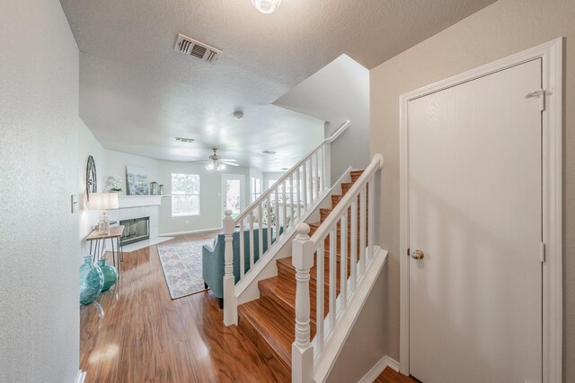 stairway featuring hardwood / wood-style floors, ceiling fan, a textured ceiling, and a tile fireplace