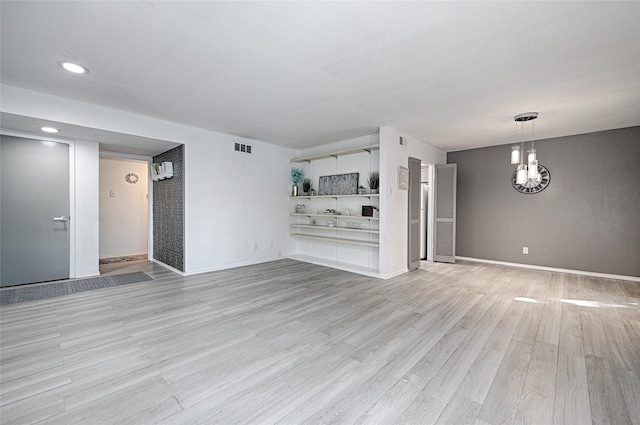 unfurnished living room featuring an inviting chandelier and light hardwood / wood-style flooring