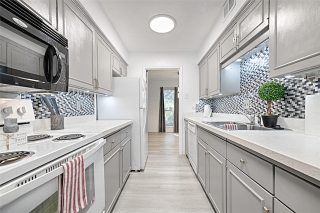 kitchen with white appliances, backsplash, sink, gray cabinets, and light wood-type flooring