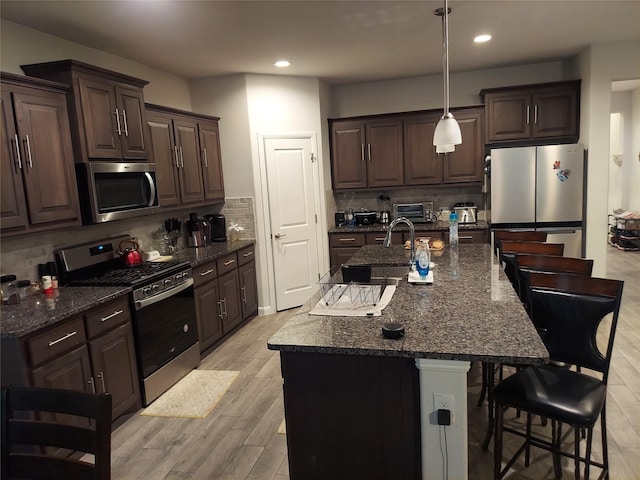 kitchen with light hardwood / wood-style floors, a kitchen bar, a kitchen island with sink, and appliances with stainless steel finishes