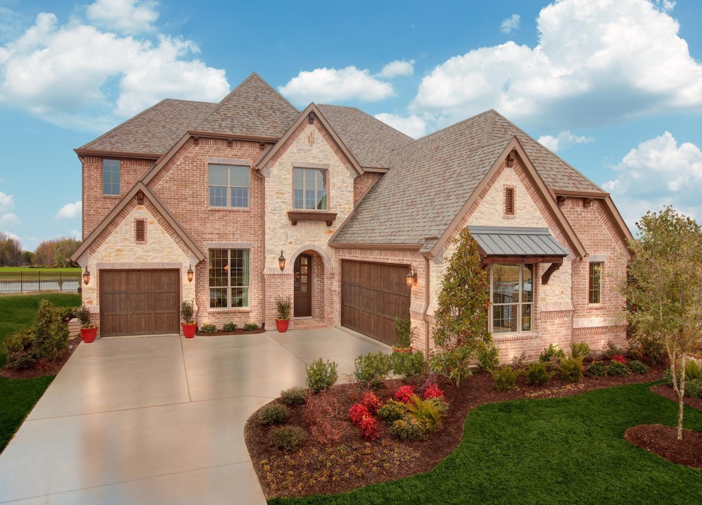 french country style house featuring a standing seam roof, brick siding, a front lawn, concrete driveway, and a shingled roof