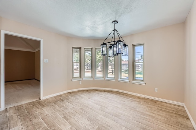 unfurnished room with a textured ceiling, a wealth of natural light, a notable chandelier, and light wood-type flooring