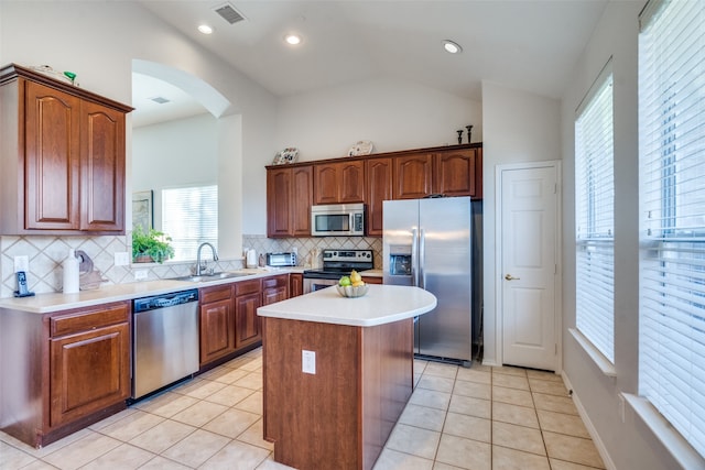 kitchen featuring stainless steel appliances, sink, light tile patterned floors, a center island, and lofted ceiling