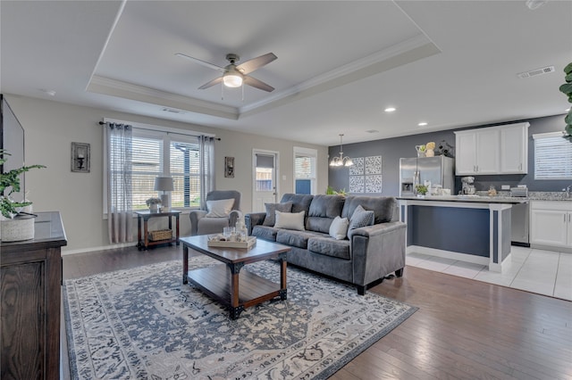 living room with crown molding, light hardwood / wood-style flooring, ceiling fan with notable chandelier, and a raised ceiling